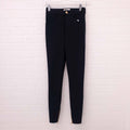 Black Celine pants hanging on a white brick wall.