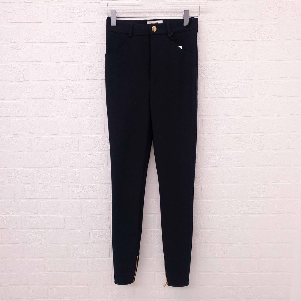 Black Celine pants hanging on a white brick wall.