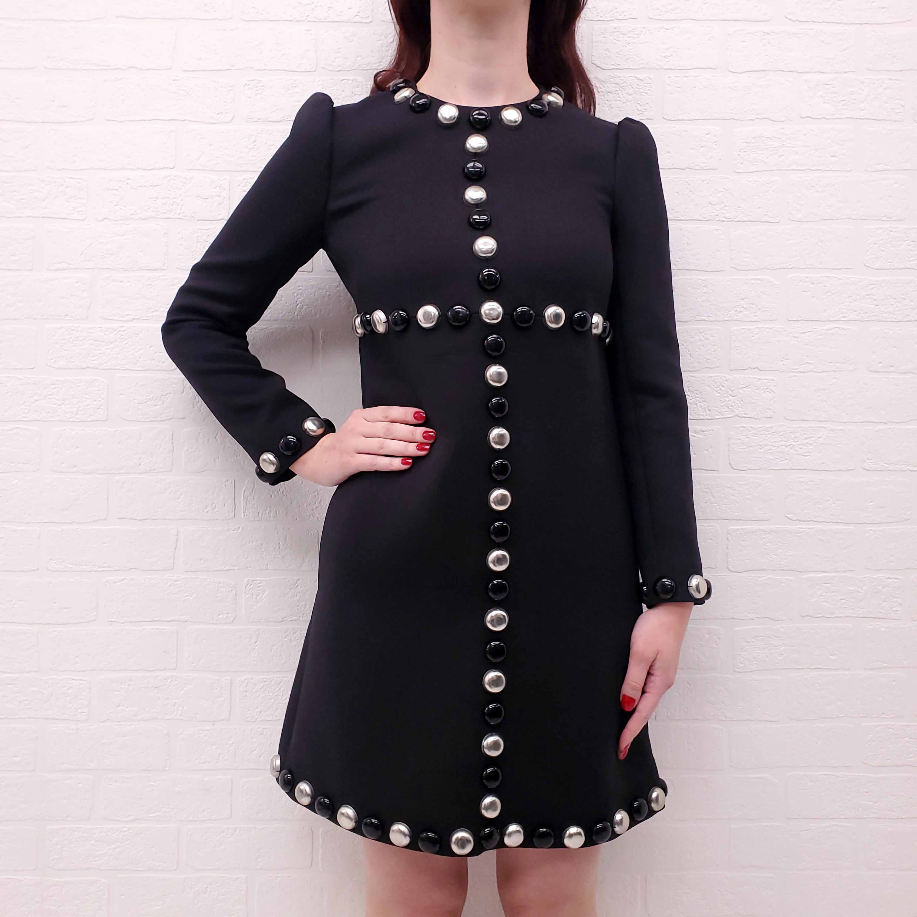 Black Celine Runway dress with silver buttons worn by a person against a white brick wall.