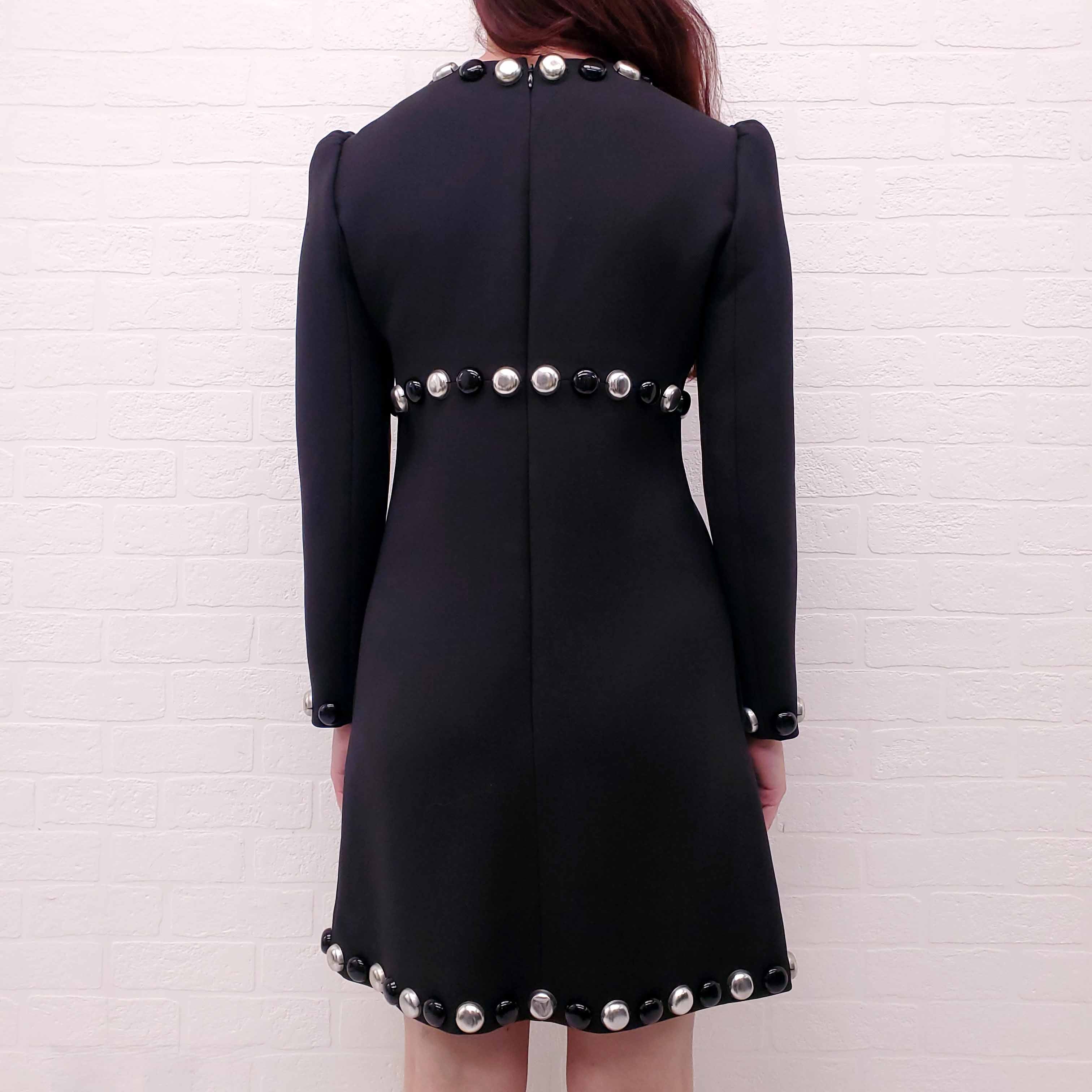 Black Celine Runway dress with silver buttons worn by a person against a white brick wall.